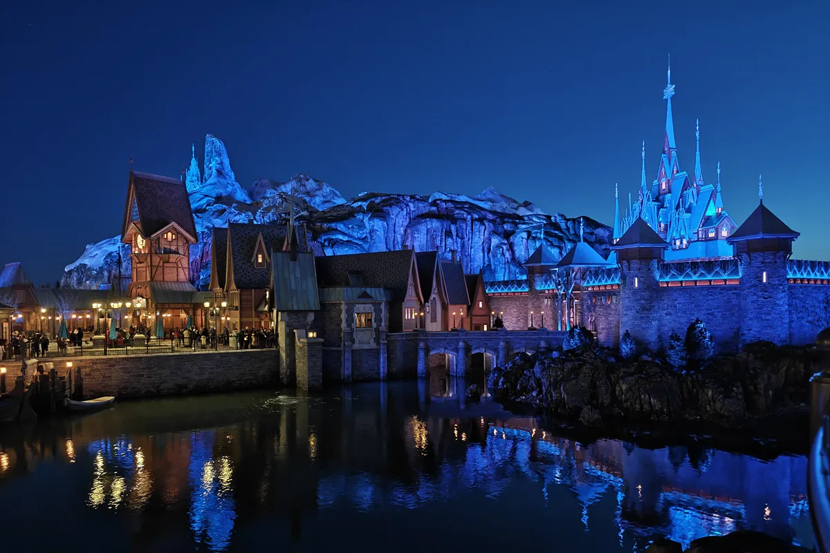 El castillo y el pueblo de Arendelle en World of Frozen de noche, con las luces reflejadas en el agua