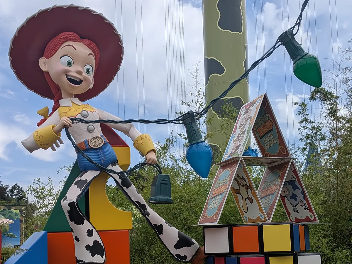 Giant Jessie statue holding a string of lights, next to the giant cards of the CARD GAME in Toy Story Playland