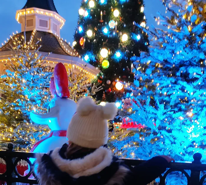 Ein Besucher betrachtet die Weihnachtsdekoration mit einem blau beleuchteten Baum in Disneyland Paris